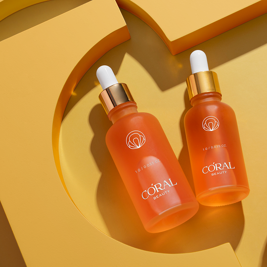 Coral Beauty serum dropper bottles styled on a warm yellow set with sculpted shadow